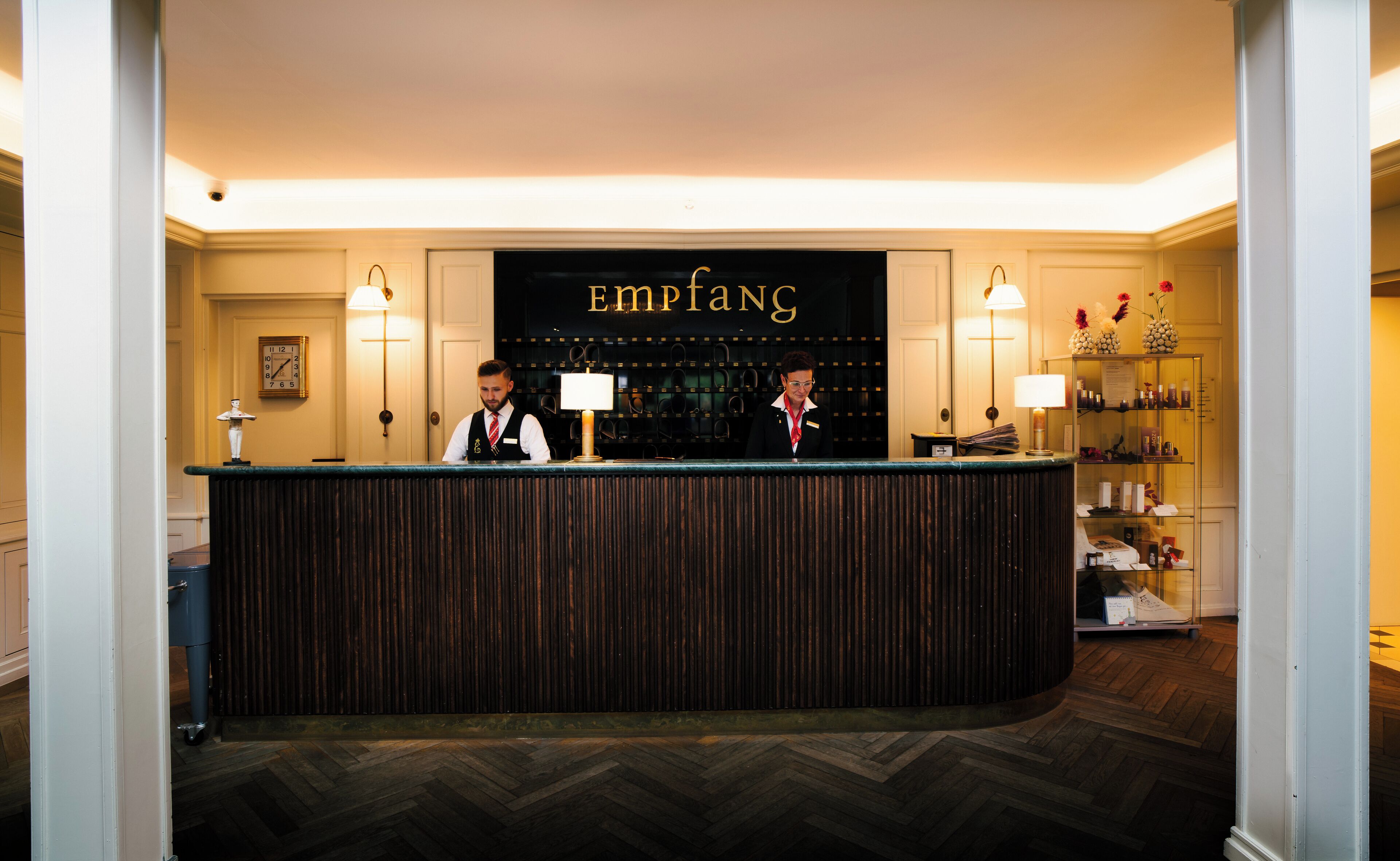 A reception desk with a sign reading "Empiang" above it, flanked by two lamps and a wall-mounted clock.