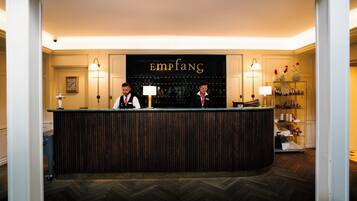 A reception desk with a sign reading "Empiang" above it, flanked by two lamps and a wall-mounted clock.
