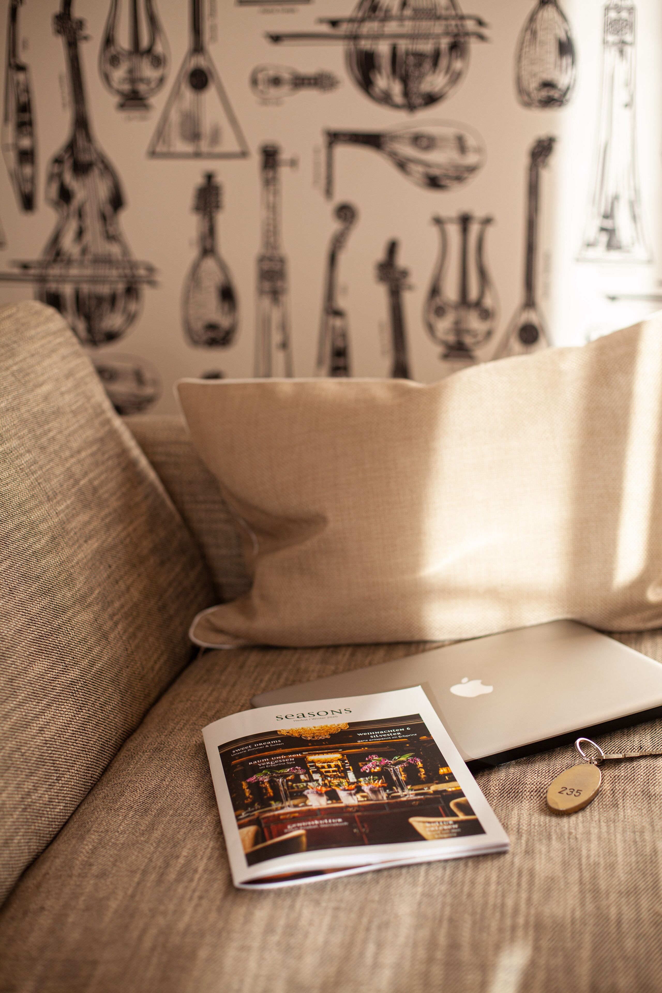 Un ordinateur portable sur un canapé beige, avec un magazine et un porte-clés.