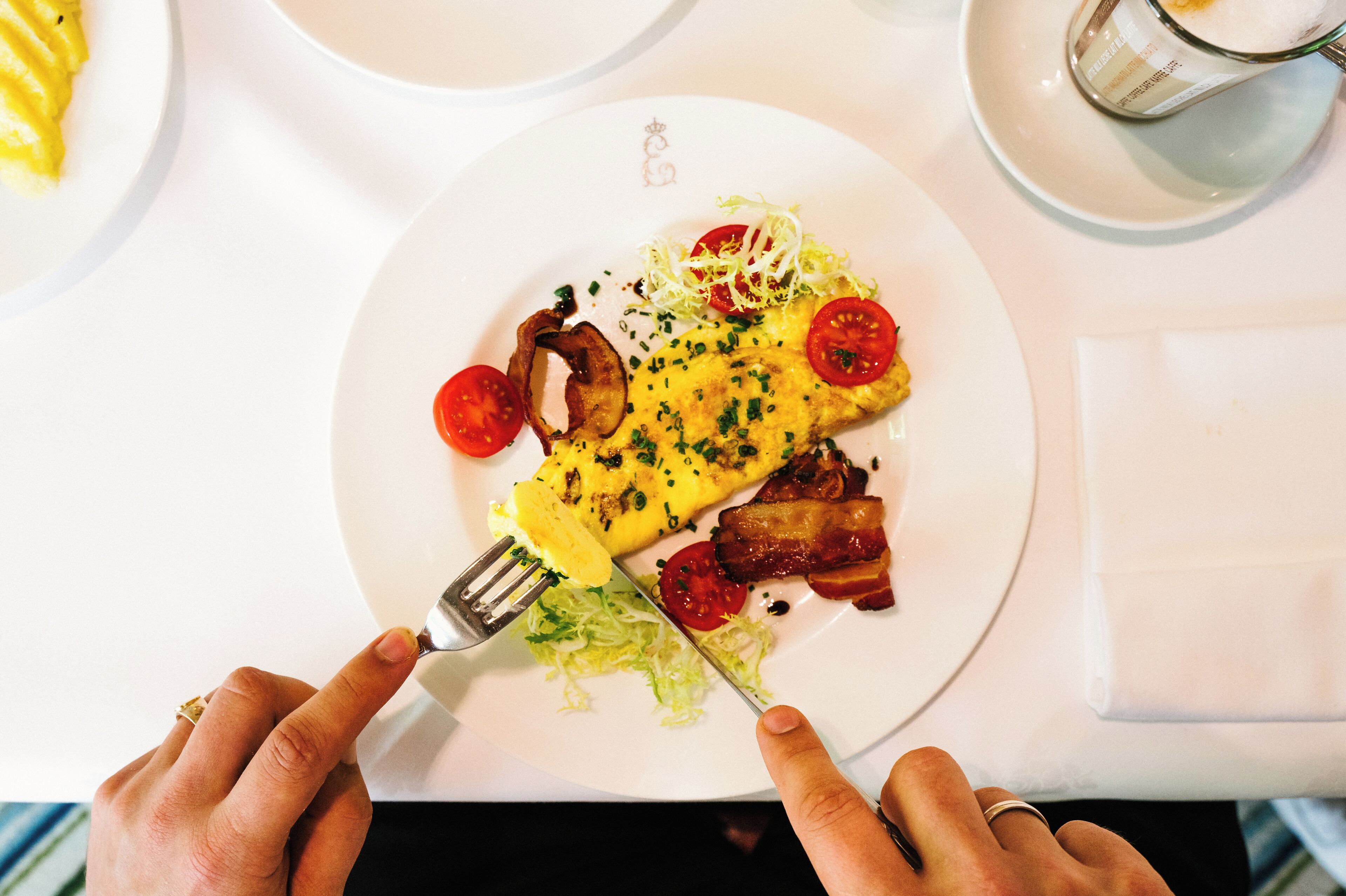 Un plato de comida con huevos, tocino, tomates y verduras de hoja verde.