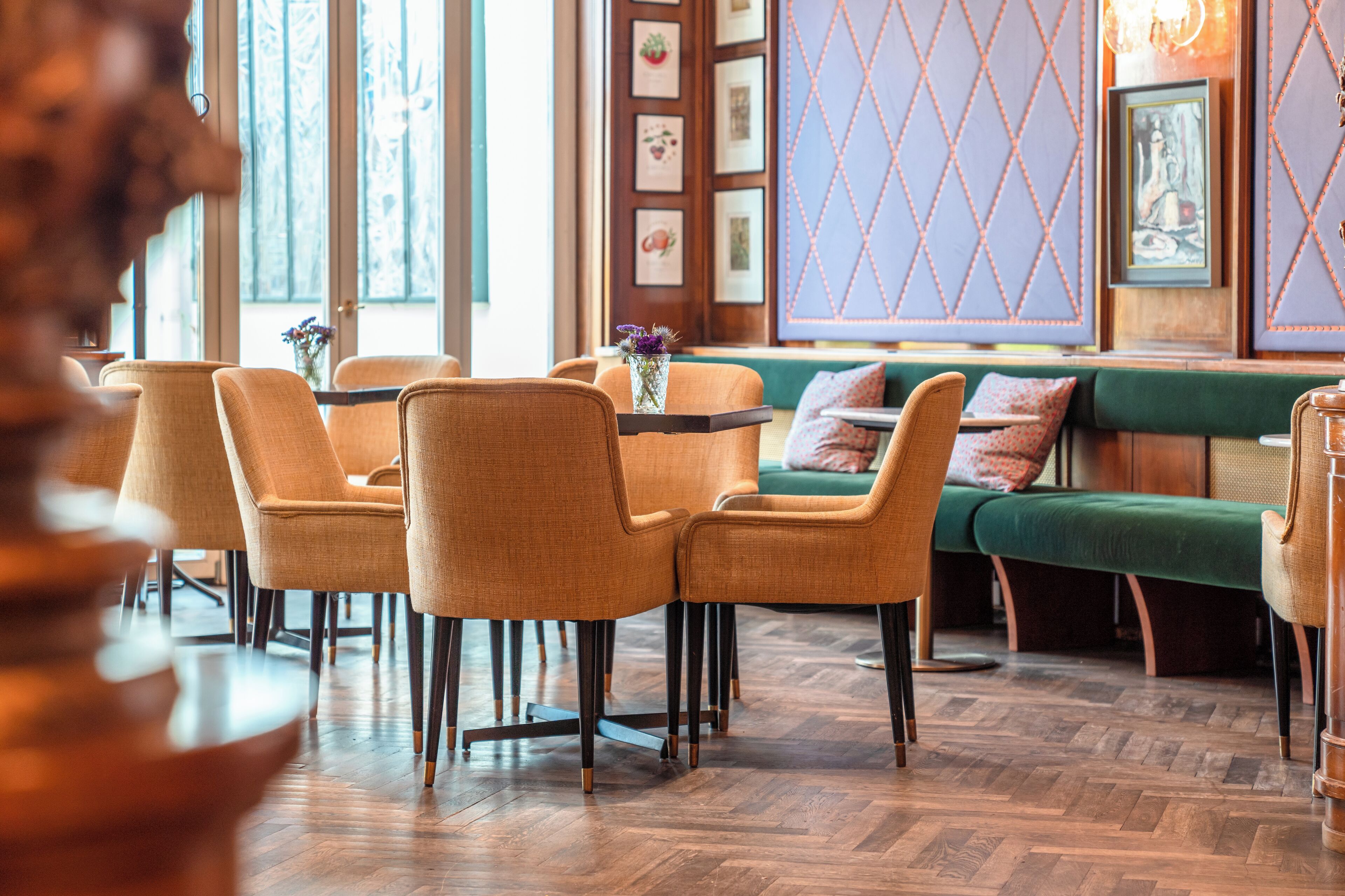 Un comedor con sillas de madera y un sofá verde, suelo de madera en patrón de espiga y una pared con cuadros enmarcados.