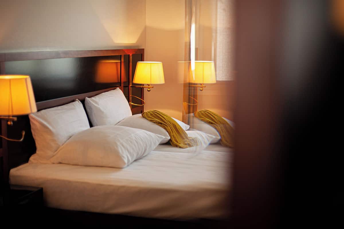 A hotel room with a neatly made bed, two bedside lamps, and a wooden headboard.