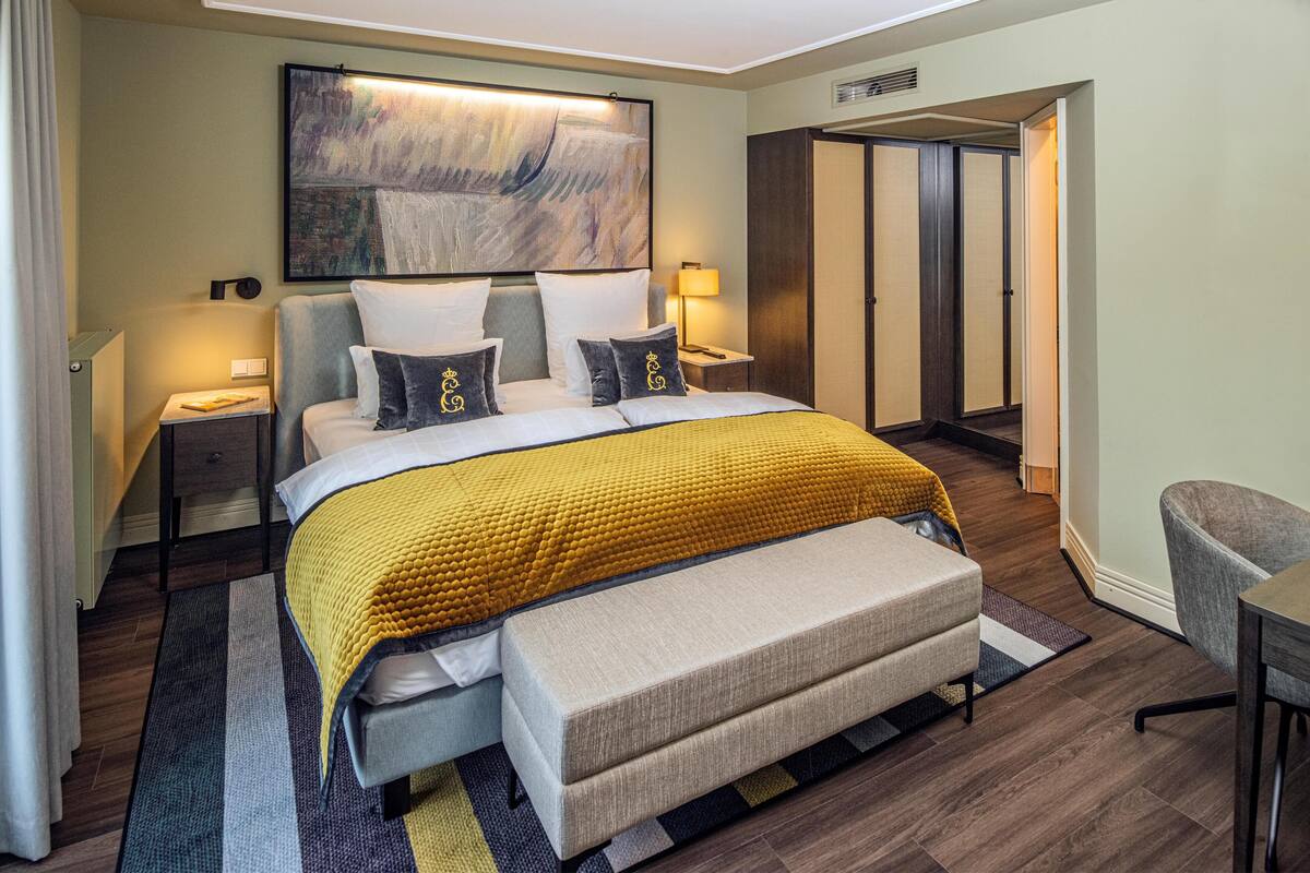 A modern hotel room with a large bed, bedside tables, a bench, and a wardrobe.