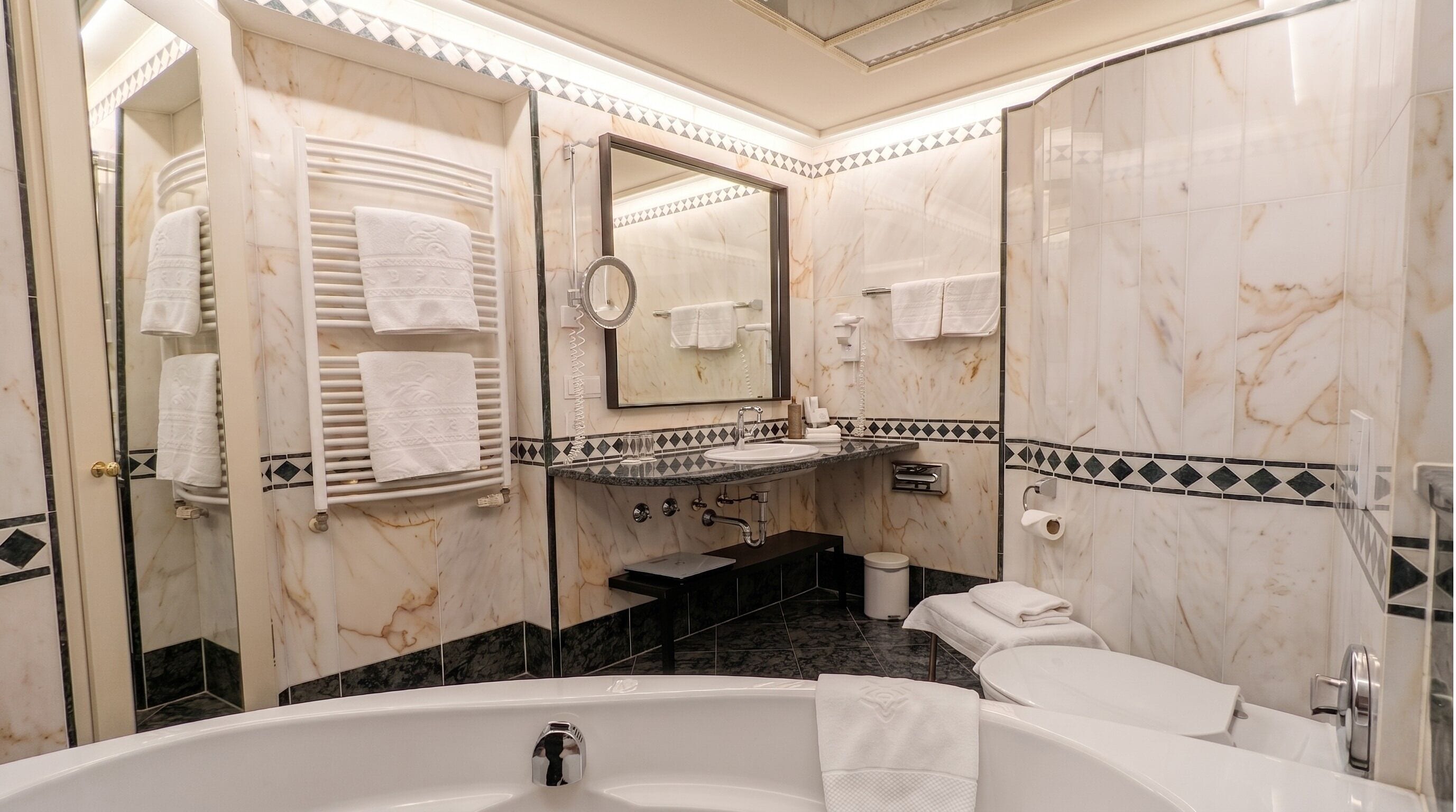 Un baño con bañera, lavamanos, espejo y toallero.