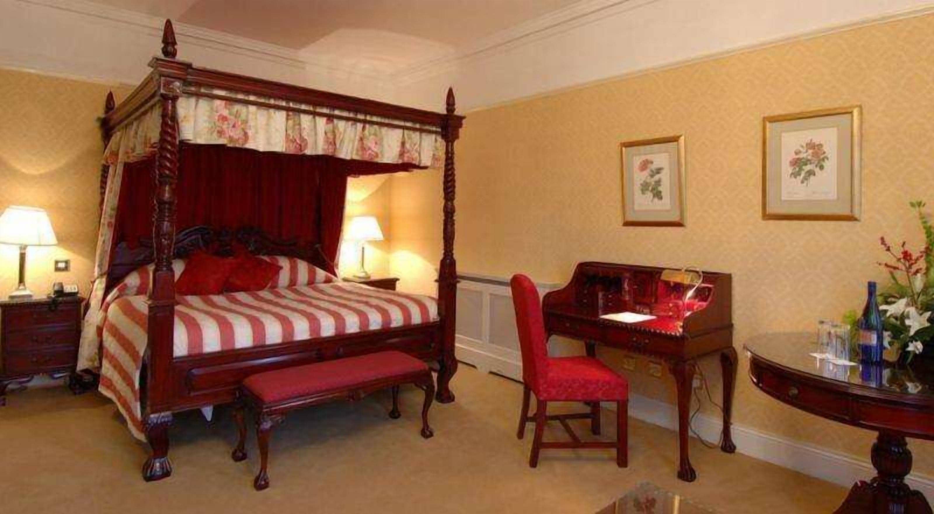 A four-poster bed with a red canopy, a desk with a chair, and two framed pictures on the wall.