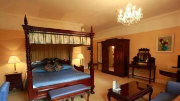 A four-poster bed with a canopy, a chandelier, a desk, and a chair in a hotel room.