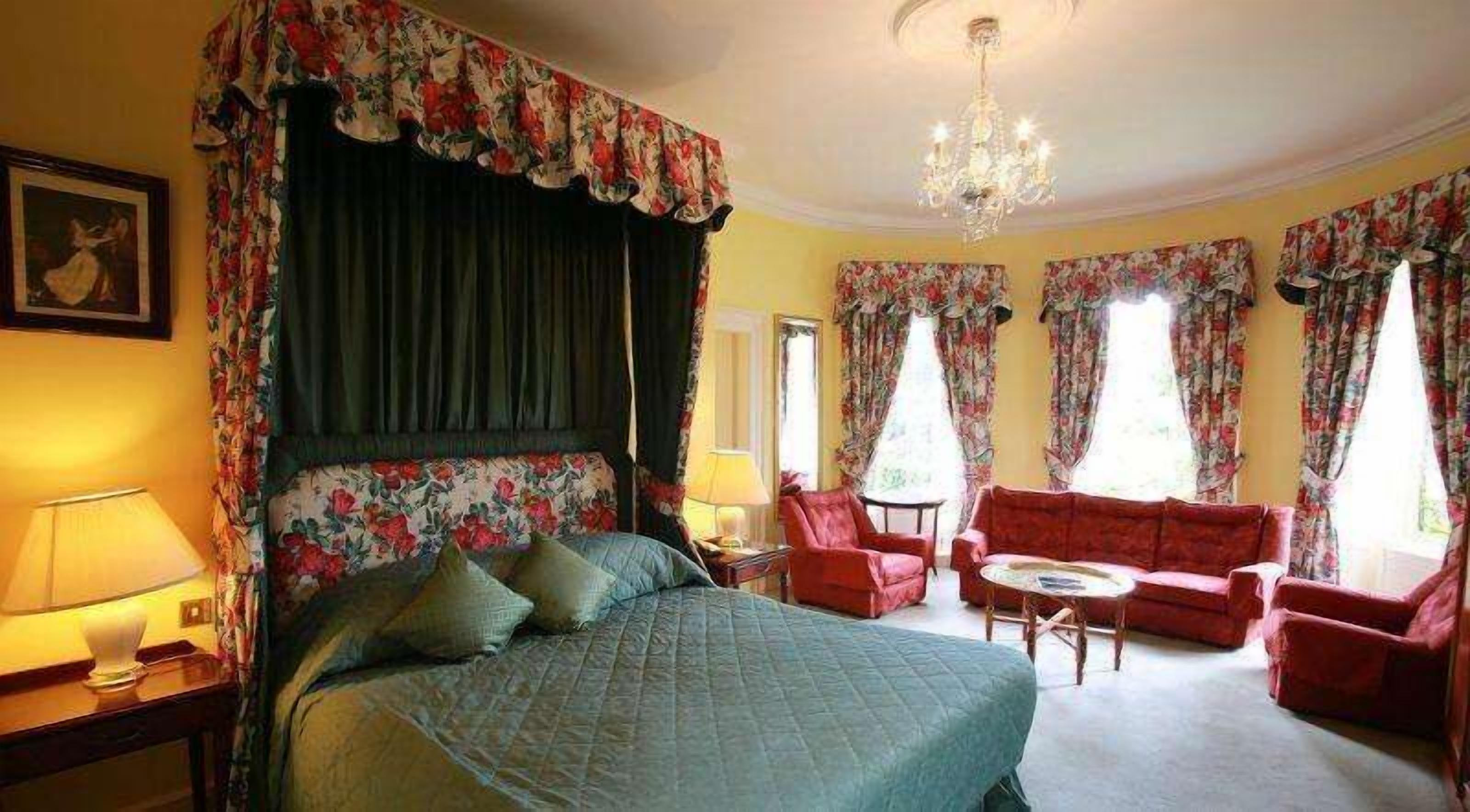 Ein Schlafzimmer mit einem Himmelbett, einem roten Sofa, einem kleinen runden Tisch und einer Chandelier.