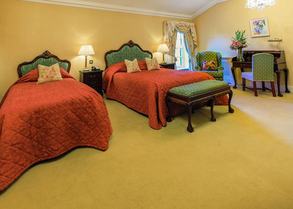 A hotel room with two beds, a bench, a desk, and a chair.