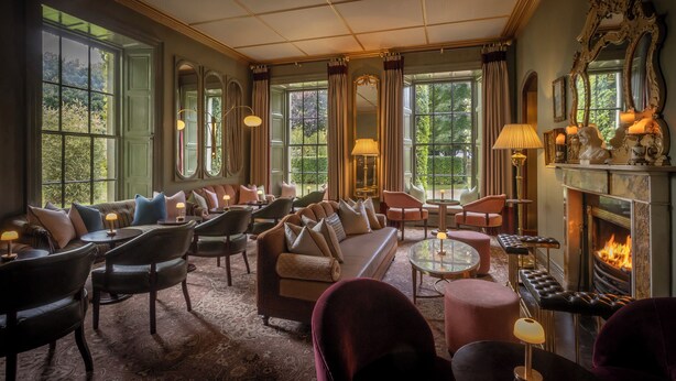 Une chambre luxueuse dotée d’une cheminée, de sièges confortables et de grandes fenêtres offrant une vue sur la verdure.
