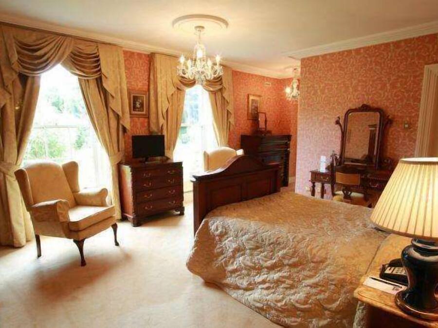 A bedroom with a large bed, a chair, a dresser, a mirror, and a lamp.