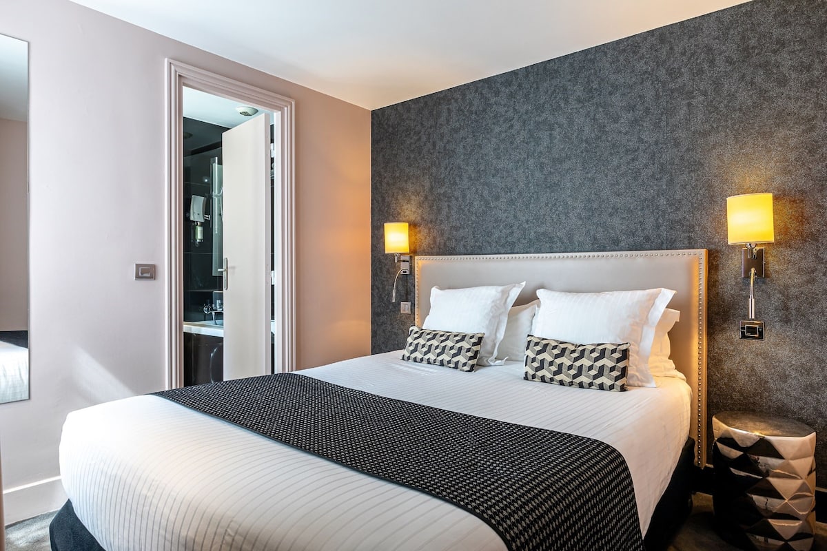 Hotelkamer met een groot bed, twee bedlampen, een kledingkast en een badkamer zichtbaar door een geopende deur.