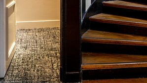 Una escalera con escalones de madera y barandilla negra, que conduce a una habitación con pared a rayas blancas y negras y una obra de arte enmarcada en la pared.