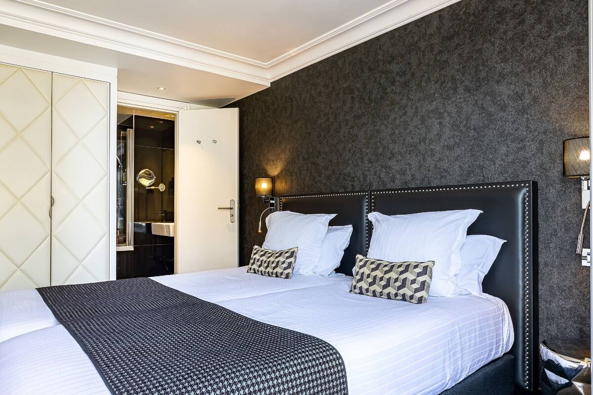 Een net opgemaakt bed met een bedsprei met patroon, een donker hoofdbord en twee decoratieve kussens.