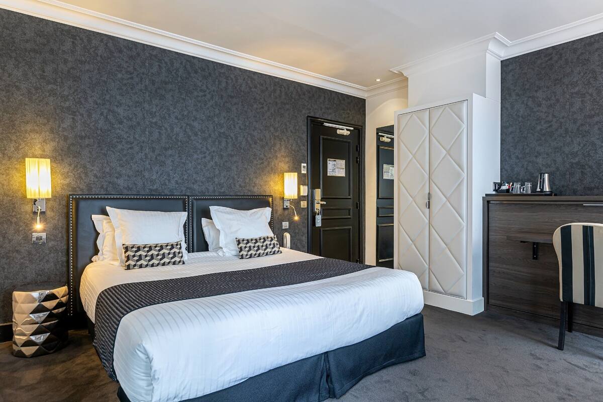 Een hotelkamer met een groot bed, nachtlampjes, een kledingkast en een bureau met een stoel.