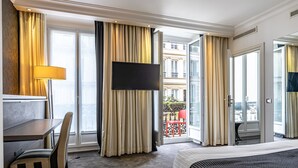 Habitación de hotel con cama, escritorio, silla, televisor y balcón con una silla roja.