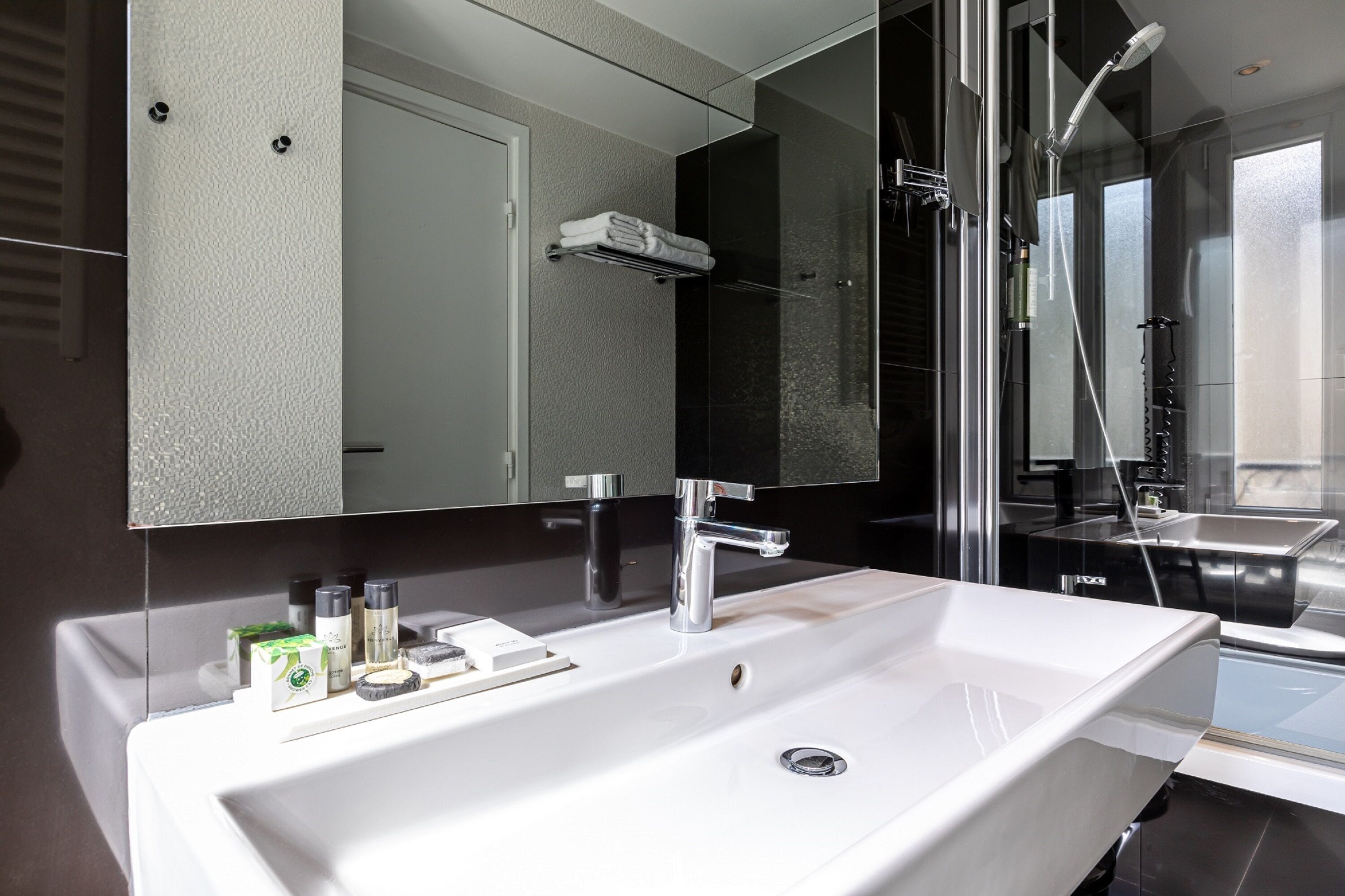 A modern bathroom with a large white sink, a mirror, and a glass-enclosed shower area.