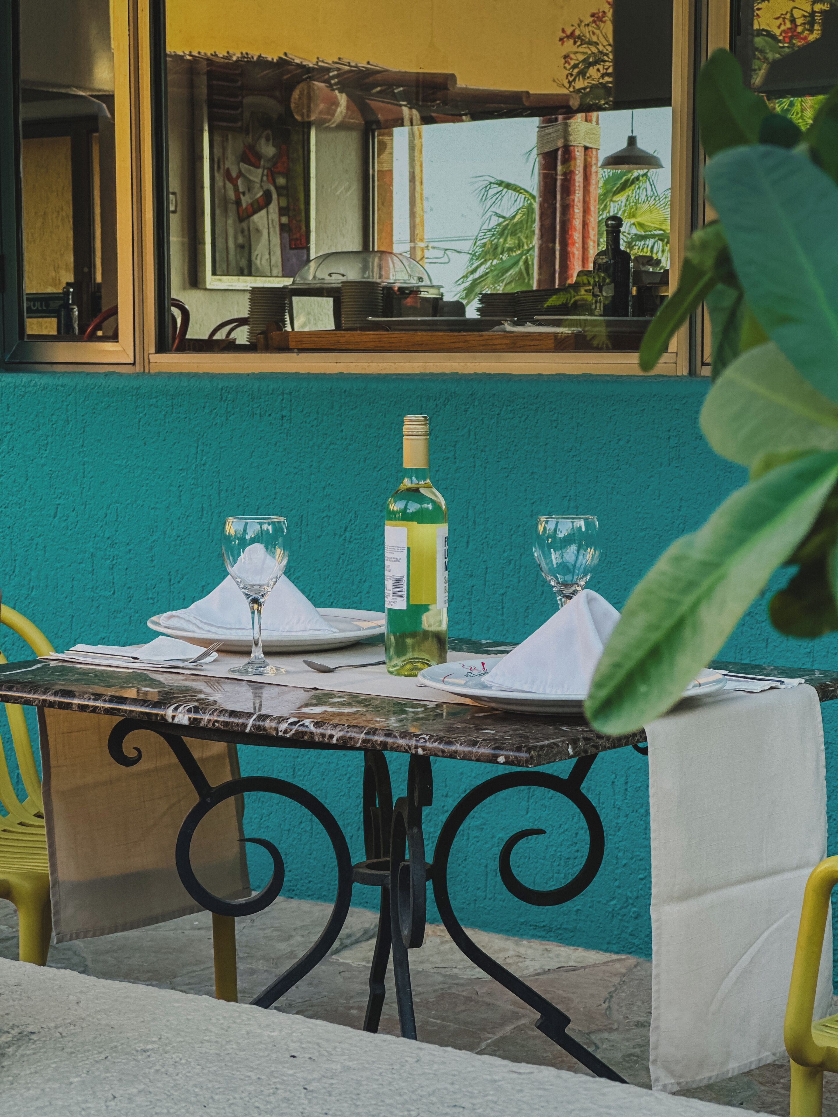 A table set for two with a bottle of white wine and two glasses, a white tablecloth, and a teal wall in the background.