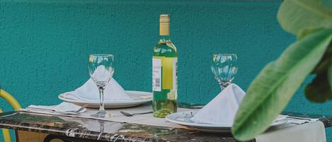 A table set for two with a bottle of white wine and two glasses, a white tablecloth, and a teal wall in the background.