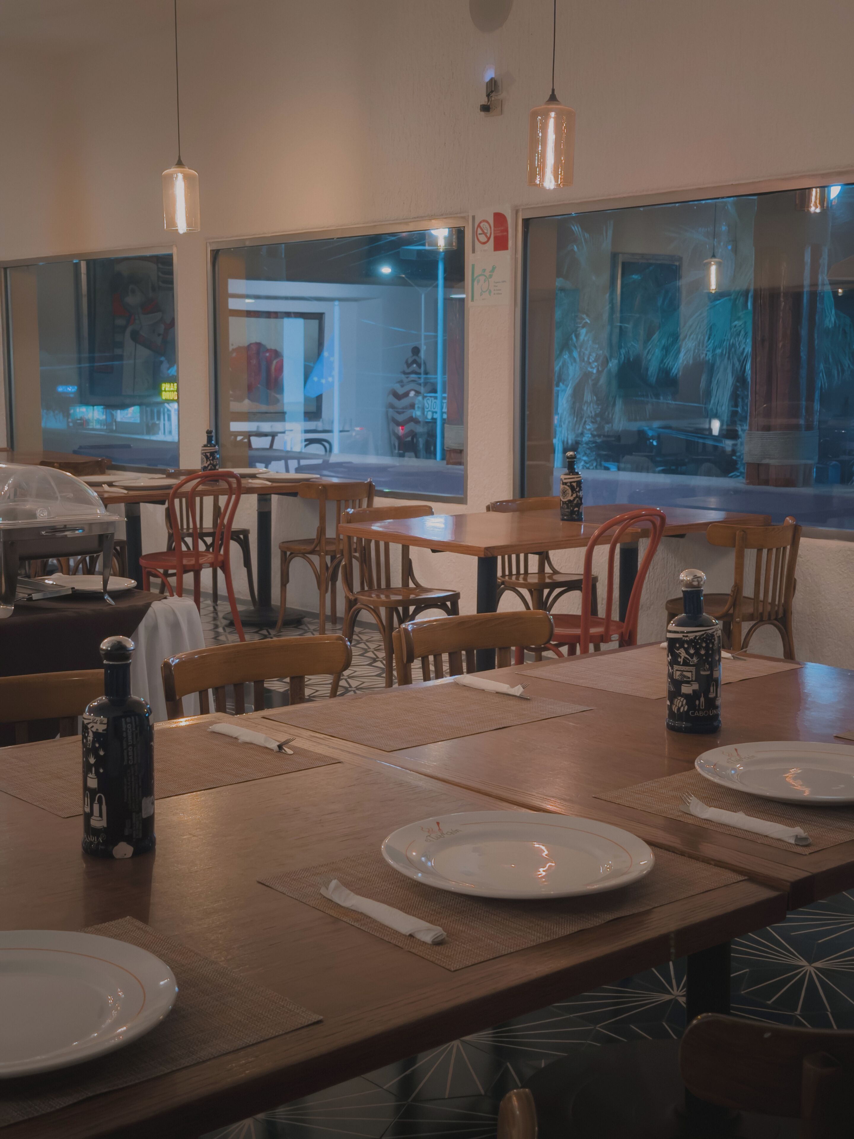 A restaurant interior with wooden tables, chairs, and a bottle of wine on the table.