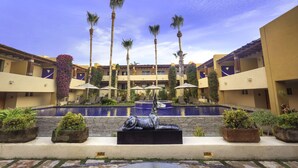 Un patio de hotel con piscina central, palmeras y una estatua.