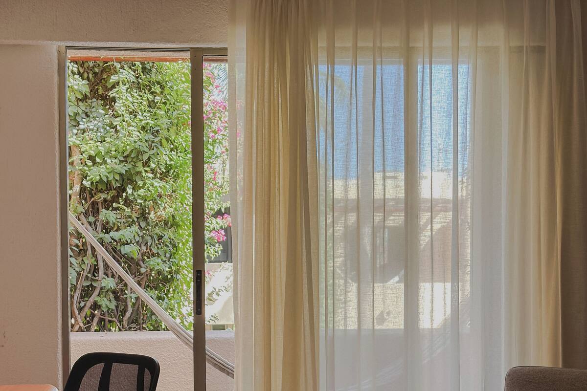 Habitación de hotel con una cama, un escritorio con silla y vistas a zonas verdes, además de una puerta corrediza de vidrio.