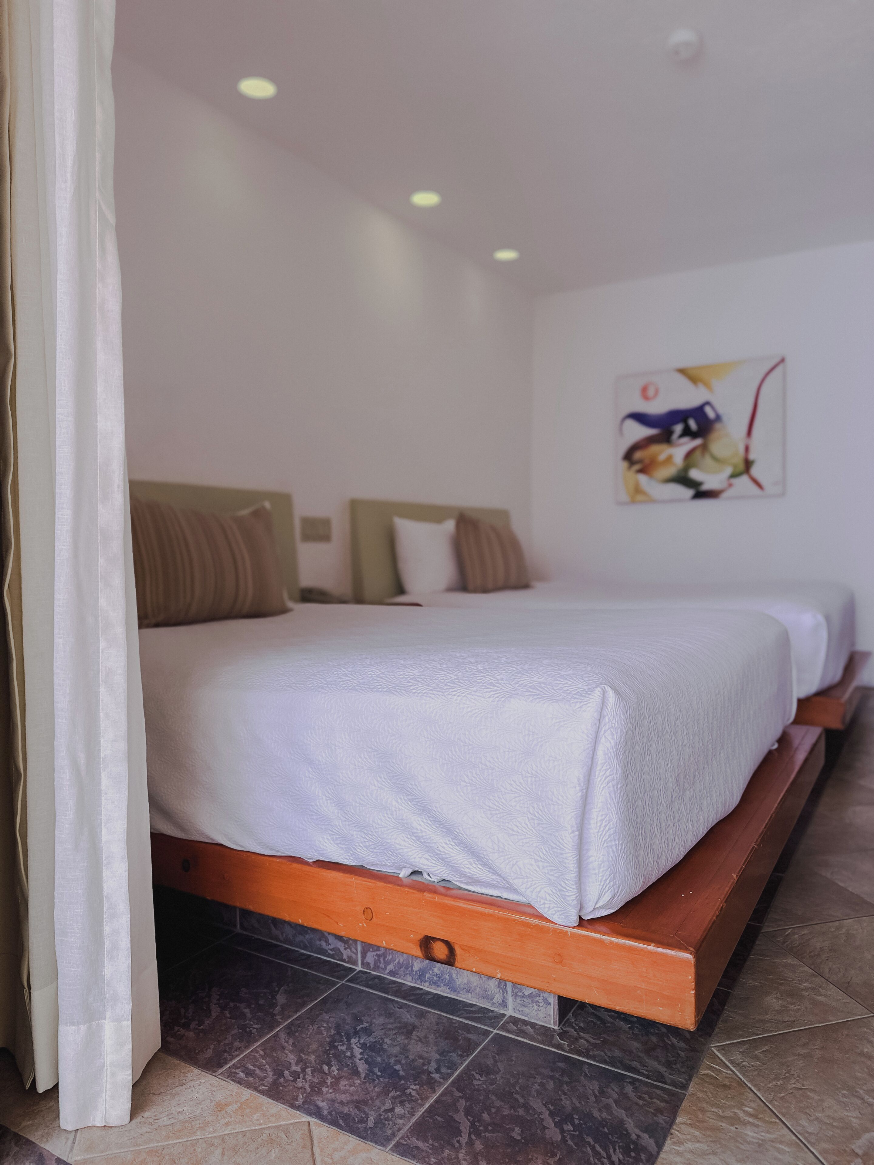 A bedroom with a bed, a headboard, a wall-mounted artwork, and a tiled floor.