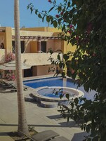 Zona de piscina con una fuente circular, sillas de descanso y una palmera.