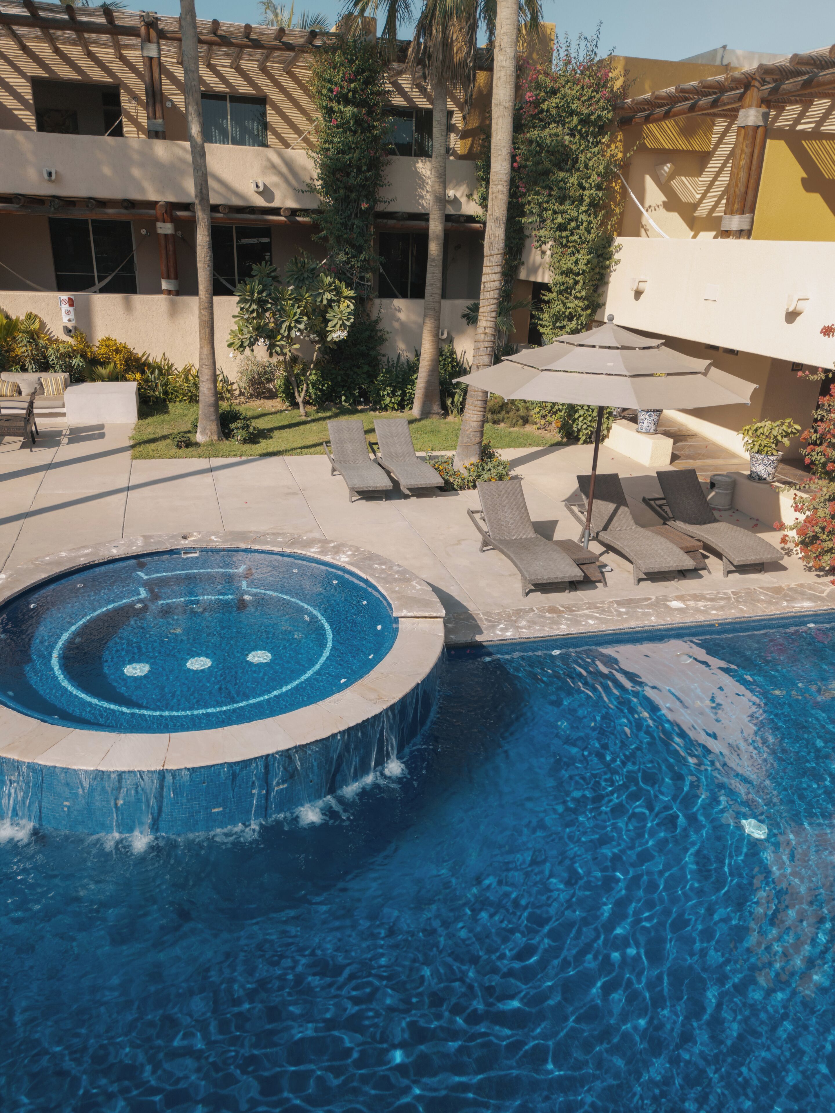 A swimming pool with a hot tub, lounge chairs, and umbrellas.