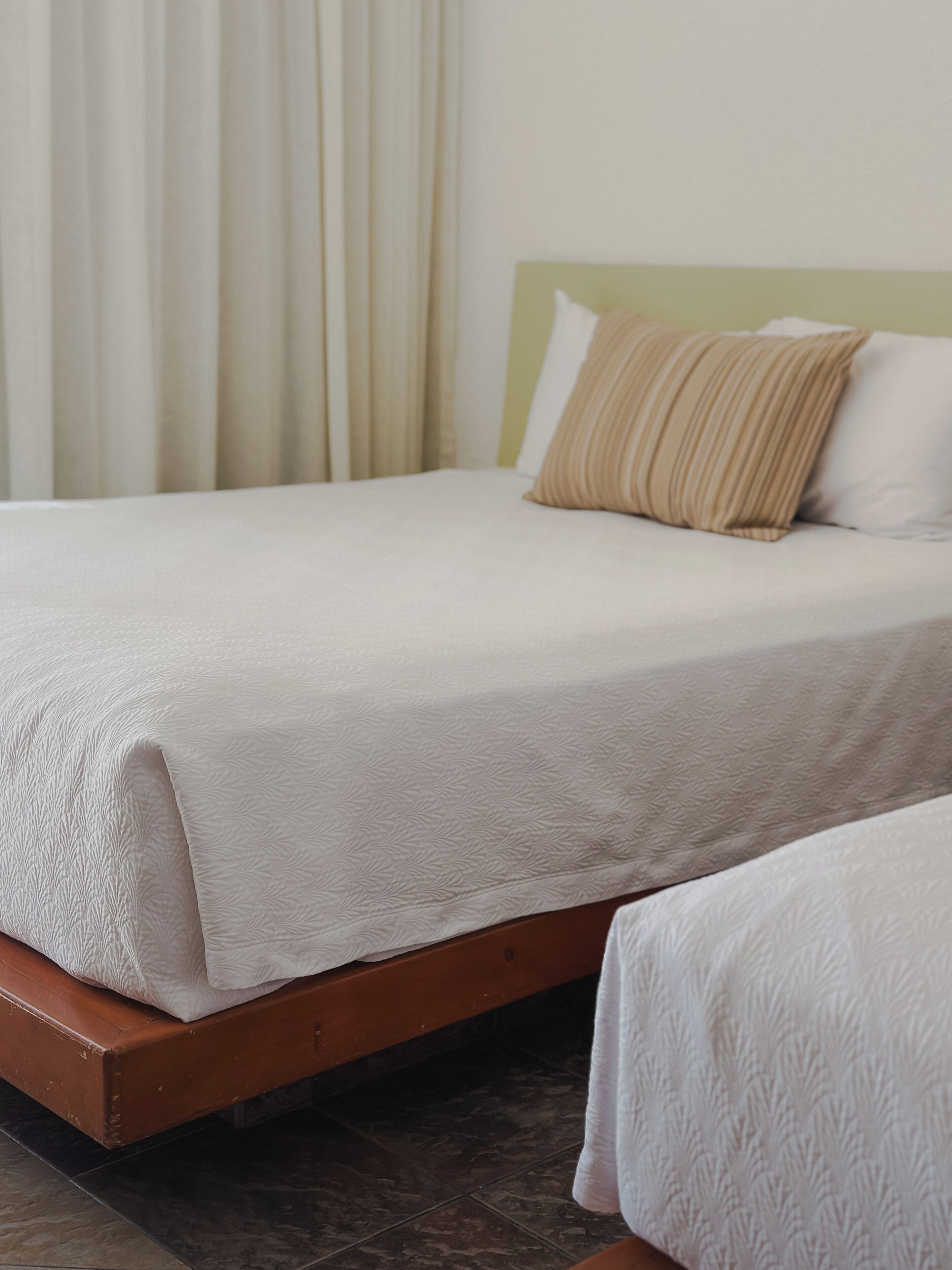A bed with a white bedspread, a wooden headboard, and a beige pillow.
