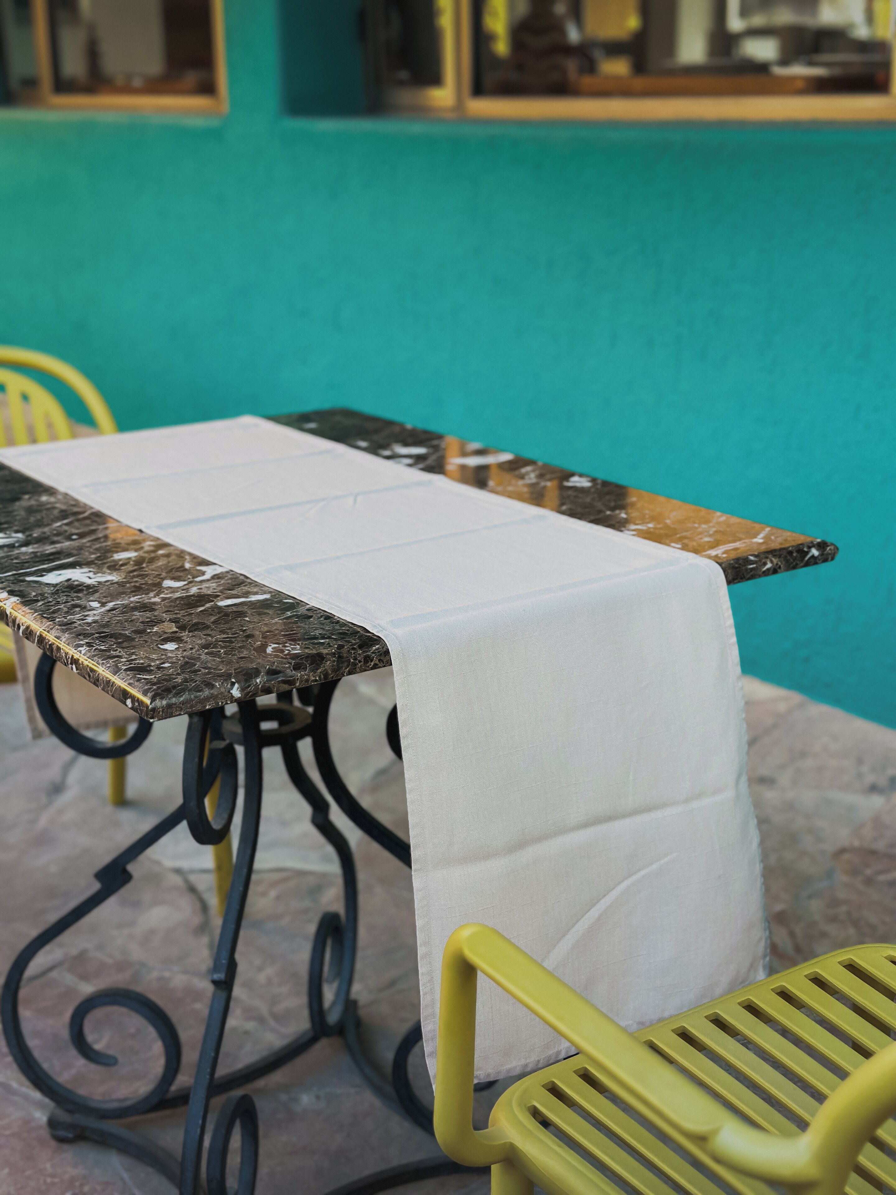 Una mesa con mantel blanco, una silla amarilla y una pared color aguamarina.