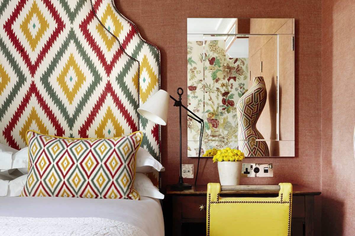 A hotel room with a bed, a desk, a chair, a lamp, and a vase with flowers.