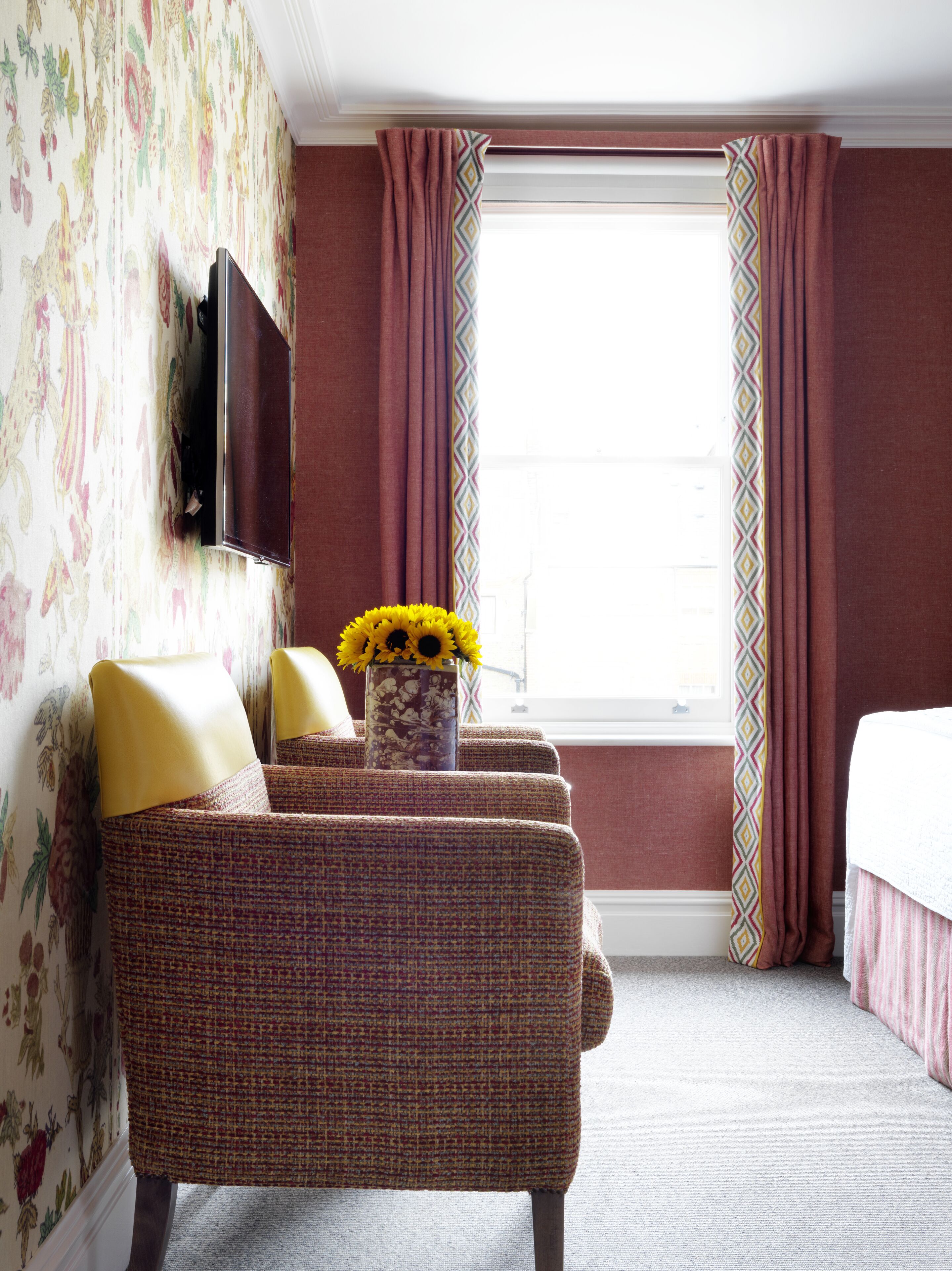 A hotel room with a sofa set, a flat-screen TV mounted on the wall, and a window with curtains.