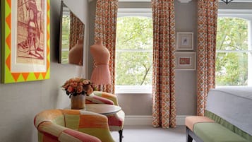 Ein Zimmer mit großem Fenster, einer Mannequin, einem Spiegel und einem gerahmten Bild an der Wand.