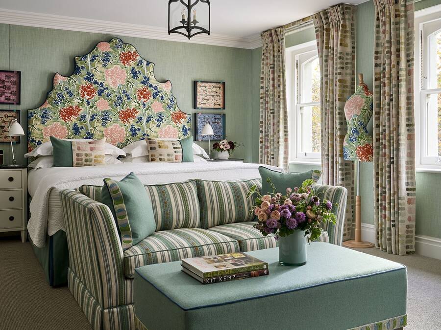 A bedroom with a large bed, a striped sofa, a bedside table, and a window with curtains.
