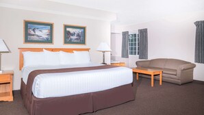 Una habitación de hotel con una cama grande, un sofá, una mesita y dos cuadros en la pared.