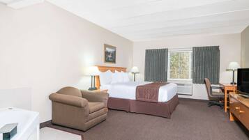 Una habitación de hotel con cama, escritorio, silla, televisor y ventana con cortinas.
