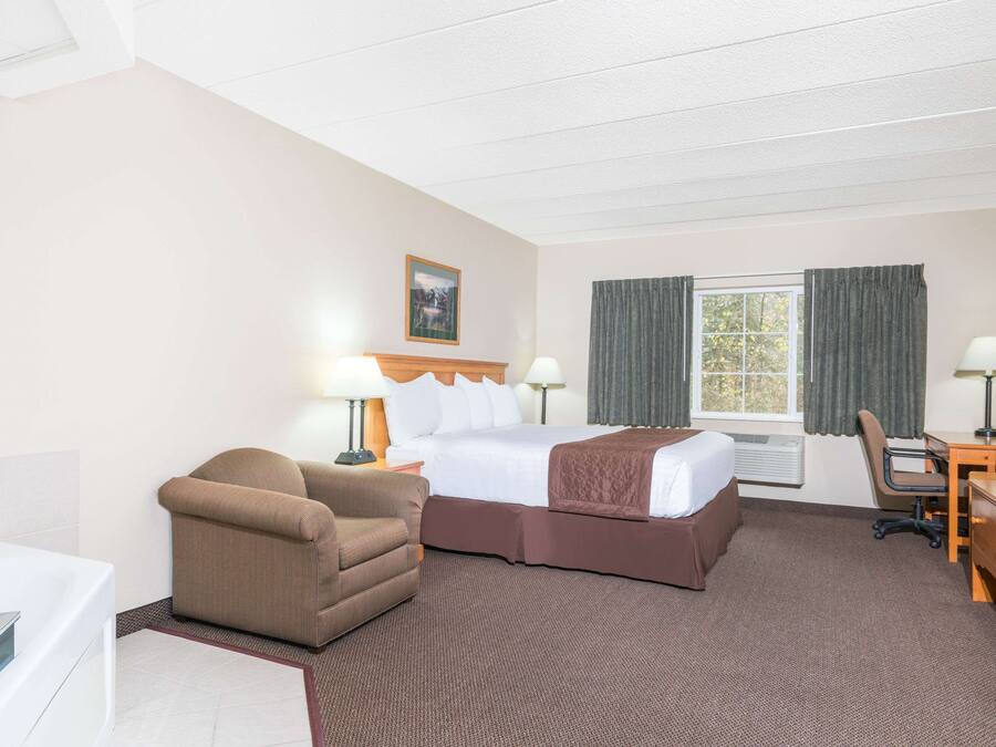 Una habitación de hotel con cama, escritorio, silla, televisor y ventana con cortinas.