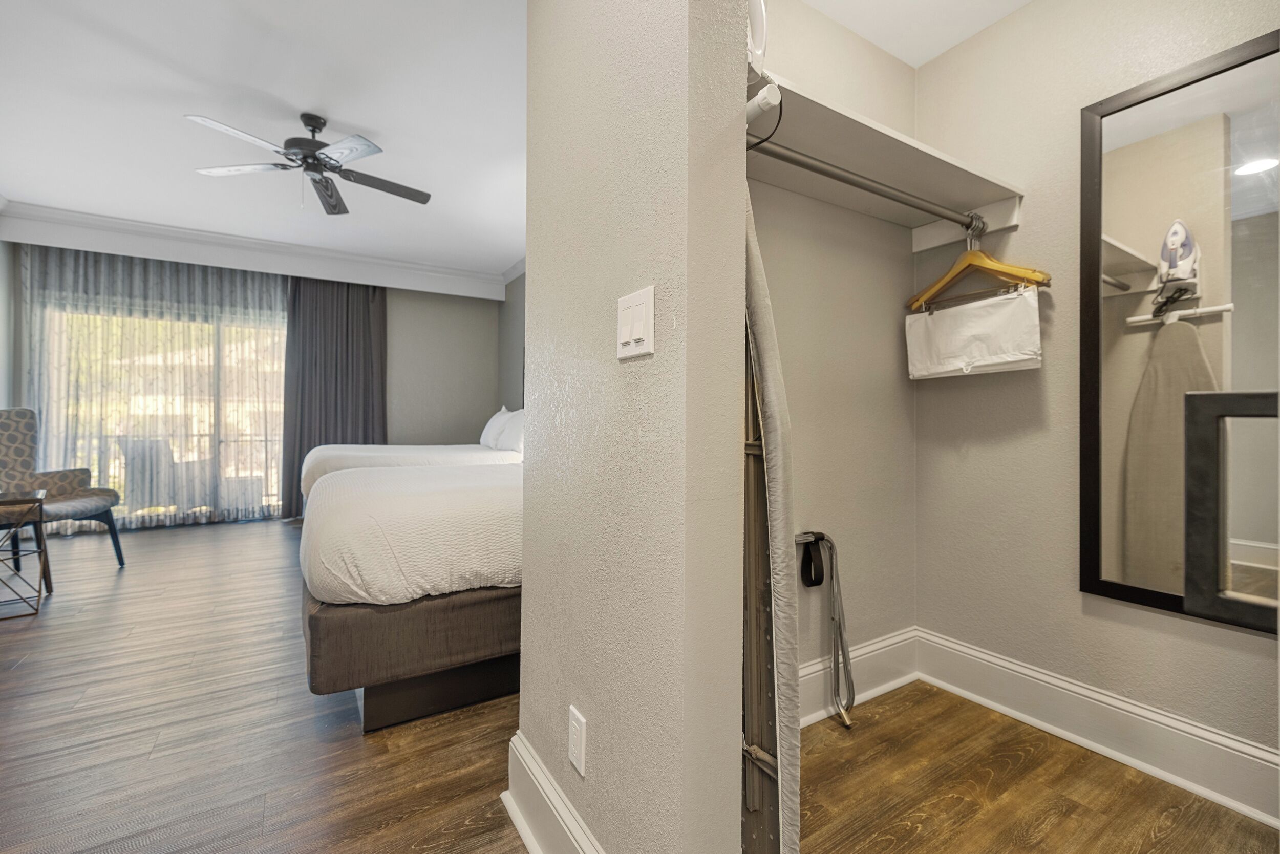 A hotel room with a bed, a ceiling fan, a mirror, and a shower area.