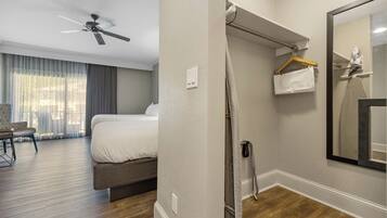 A hotel room with a bed, a ceiling fan, a mirror, and a shower area.
