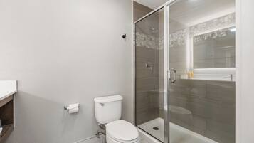 Un baño con inodoro, ducha con cerramiento de vidrio y lavamanos blanco.