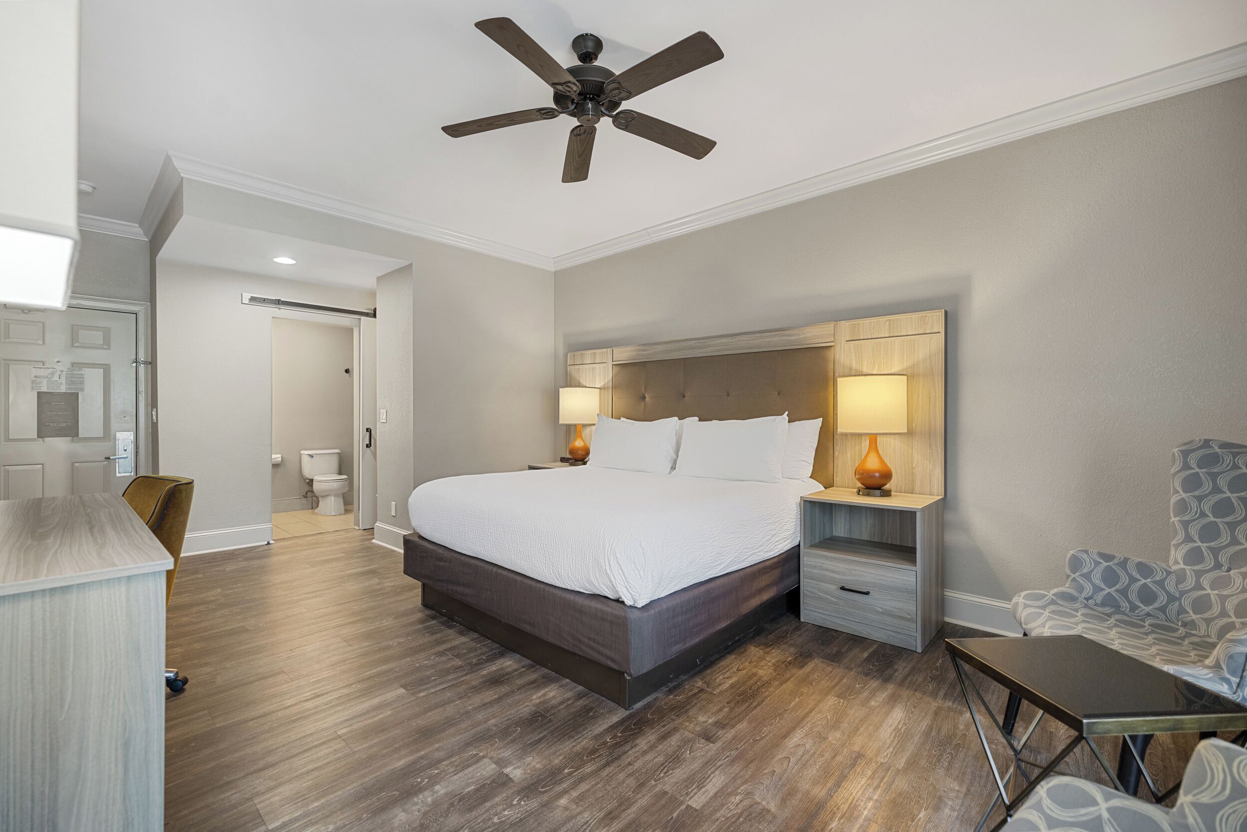 A modern bedroom with a large bed, wooden headboard, bedside lamps, and a ceiling fan.