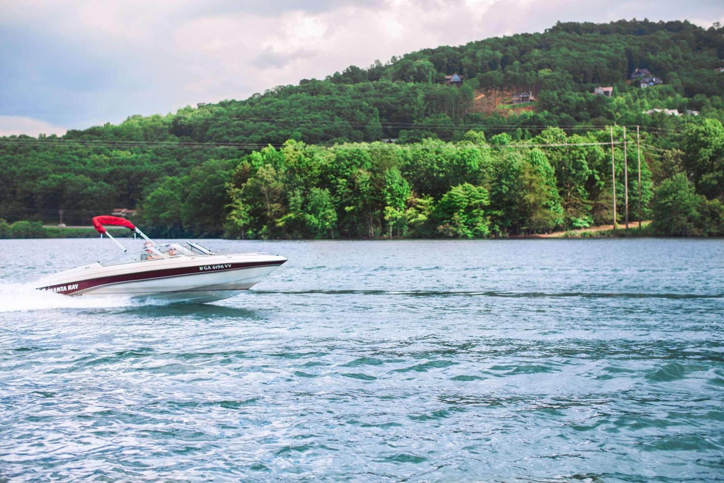 A speedboat on a lake with a forested hillside in the background.