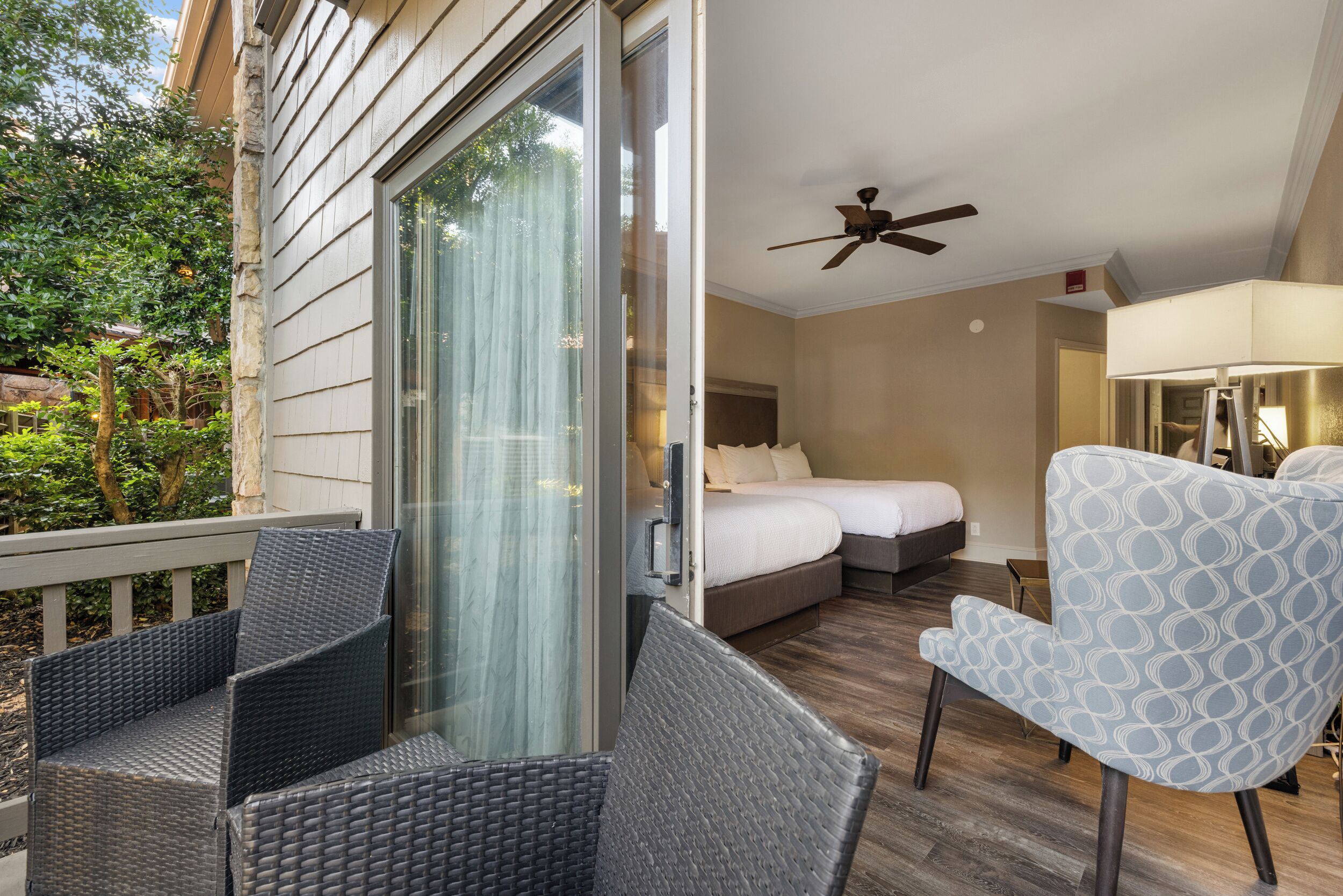A hotel room with a bed, a ceiling fan, a chair, and a view of the outdoors.