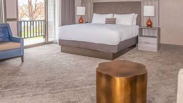 A hotel room with a large bed, two bedside tables with lamps, a blue armchair, and a gold side table.