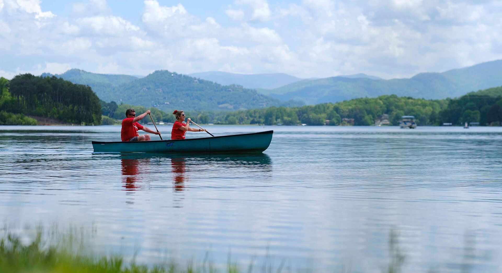 Dos personas remando en un lago tranquilo con montañas al fondo.