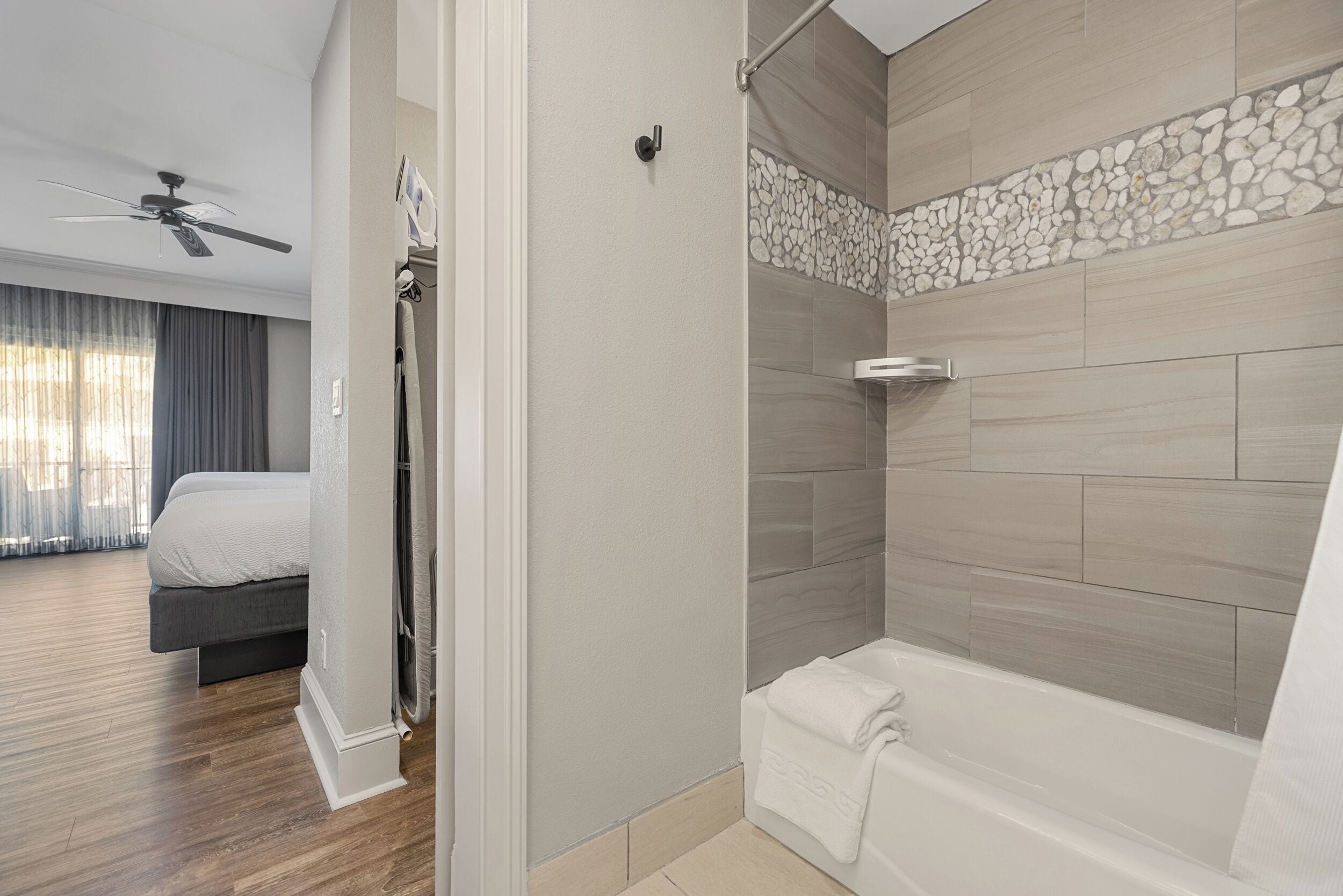 A modern bathroom with a bathtub, shower, and a ceiling fan.