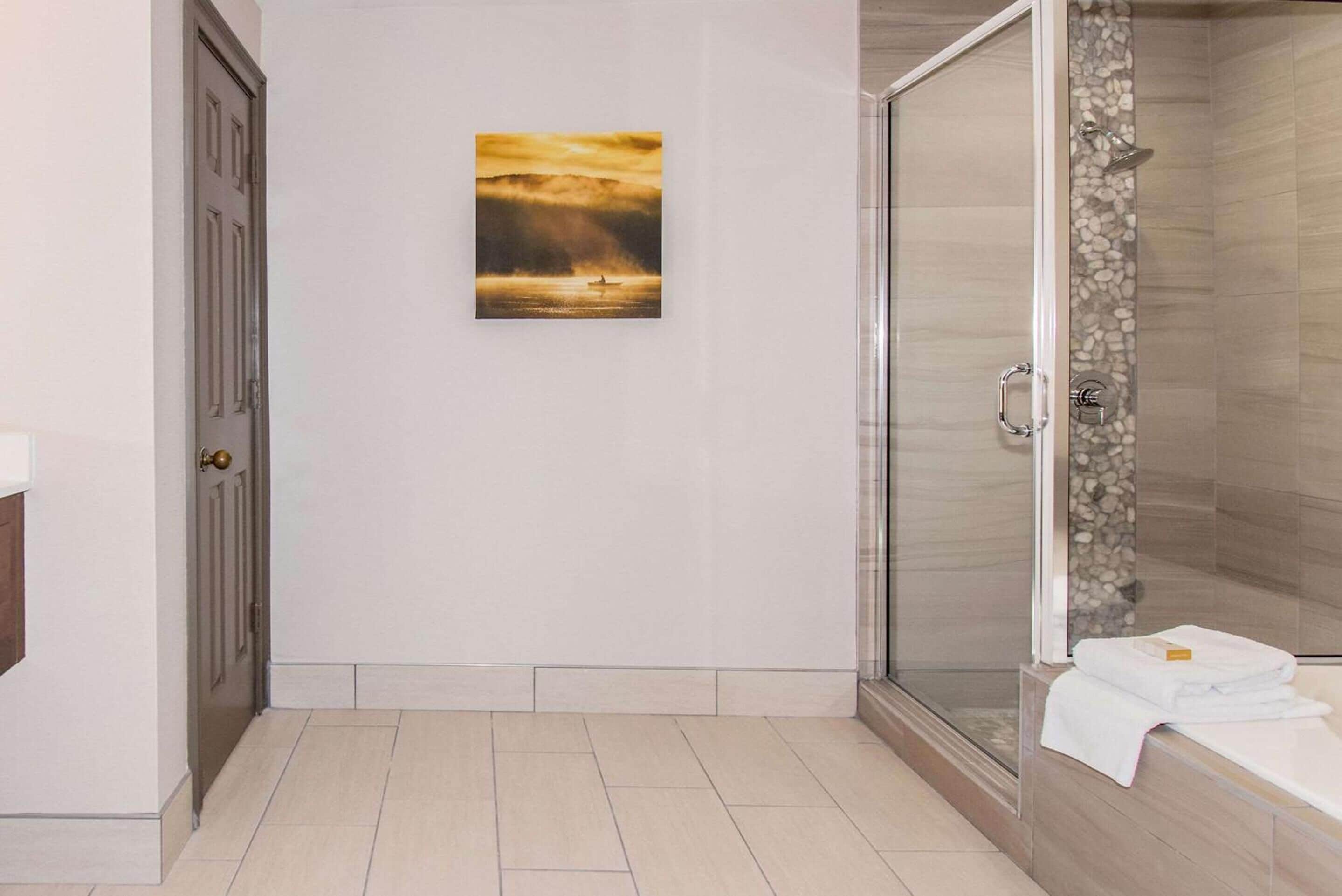 Un baño con ducha de vidrio, una puerta y un cuadro en la pared.