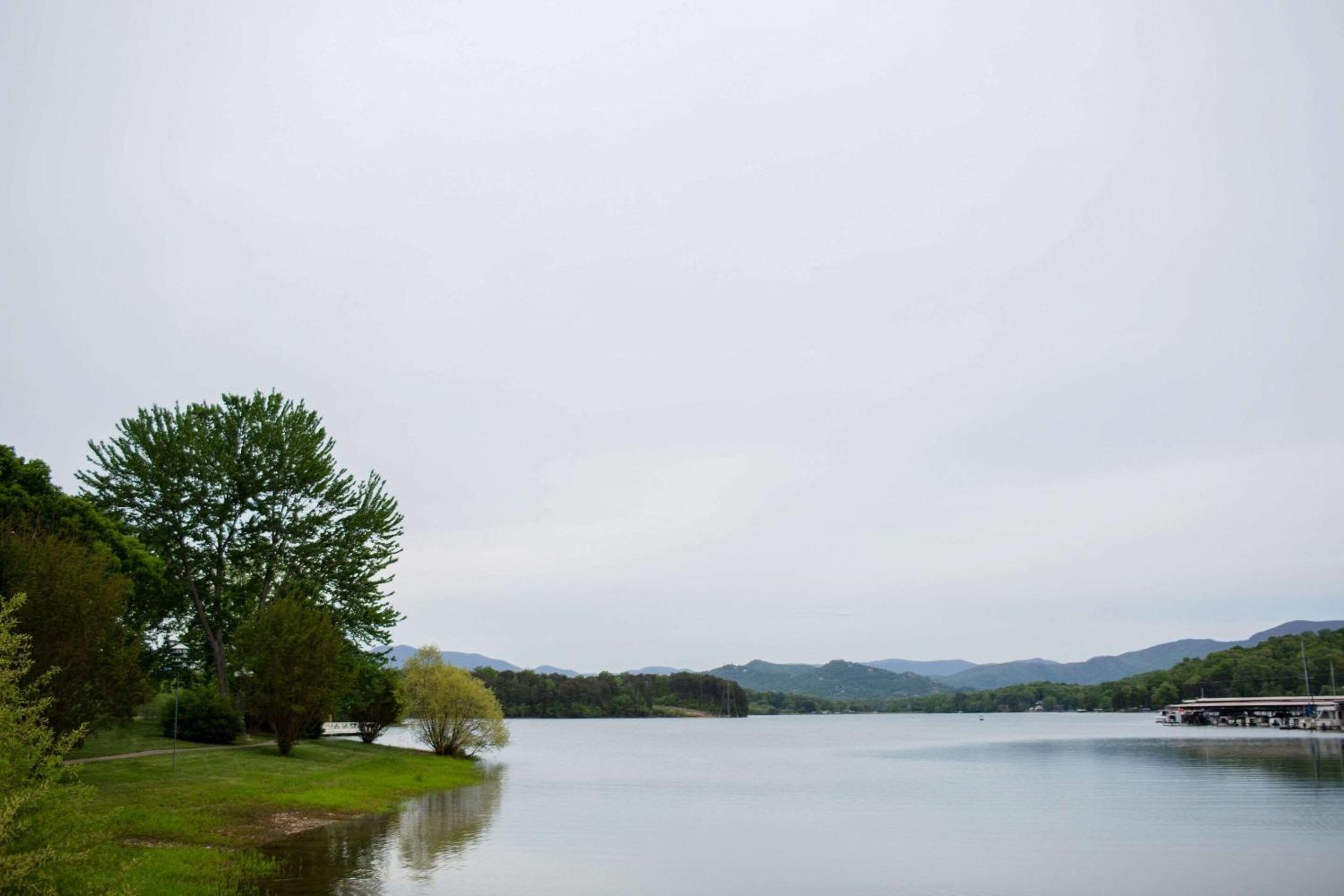 Un lago tranquilo con un muelle, rodeado de vegetación y colinas.