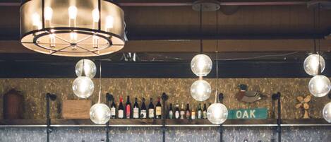 A bar with multiple shelves of liquor bottles, a sign labeled "OAK", and hanging spherical light fixtures.