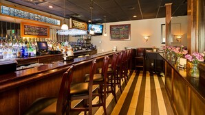 A bar area with a long counter, multiple stools, a television mounted on the wall, and a menu board listing various drinks.